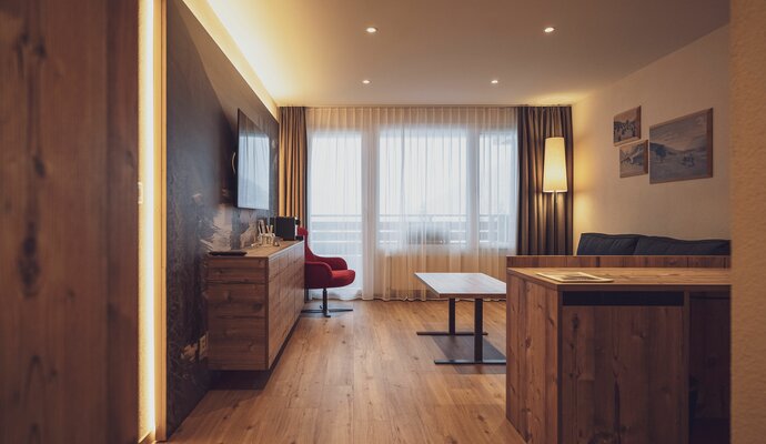 Large room with wooden floor, sofa, wooden chest of drawers and TV | © Davos Klosters Mountains 