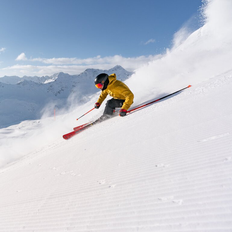 Skifahrer gleitet fröhlich den Hang hinunter, umgeben von schneebedeckten Bergen und klarem Himmel. | © Arosa Lenzerheide 