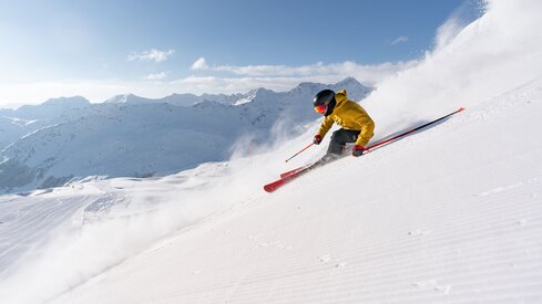 Skifahrer gleitet fröhlich den Hang hinunter, umgeben von schneebedeckten Bergen und klarem Himmel. | © Arosa Lenzerheide 